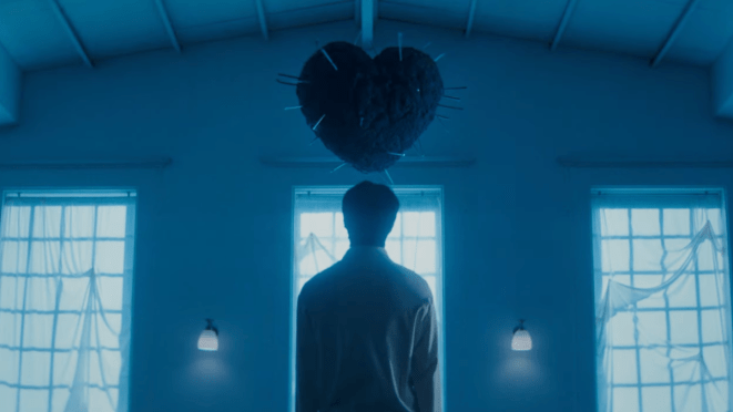 Review do álbum Unfold do Monsta X: cena do MV de "heal" com um dos membros de costas, olhando para um coração cheio de pregos