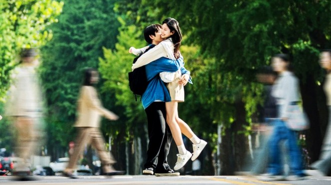 Review do K-Drama Still Shining: personagens de Jin Young (Yeon Tae Seo) e Kim Min Ju (Mo Eun A) em um abraço no meio da rua, com pessoas fora de foco passando ao fundo