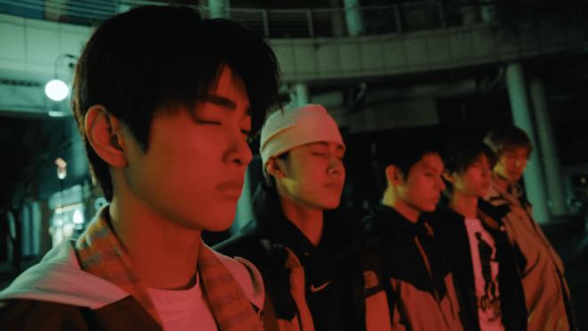 Review do álbum GREENGREEN do CORTIS: cena do MV da title "REDRED" com  James, Juhoon, Keonho, Martin e Seonghyeon iluminados por uma luz baixa vermelha e de olhos fechados