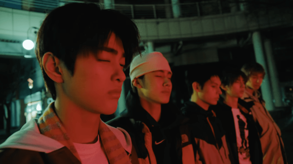Review do álbum GREENGREEN do CORTIS: cena do MV da title "REDRED" com James, Juhoon, Keonho, Martin e Seonghyeon iluminados por uma luz baixa vermelha e de olhos fechados