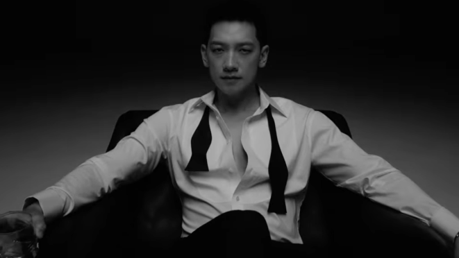 Review do single "Feel It" do Rain: cena em preto e branco do MV com ele sentado em uma poltrona, segurando um copo de whisky