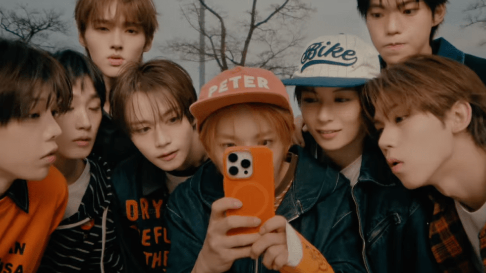 Review do álbum de debut do YUHZ, Orange Record: cena do MV de "Rush Rush" com todos os membros reunidos olhando para a câmera do celular nas mãos do Sechan